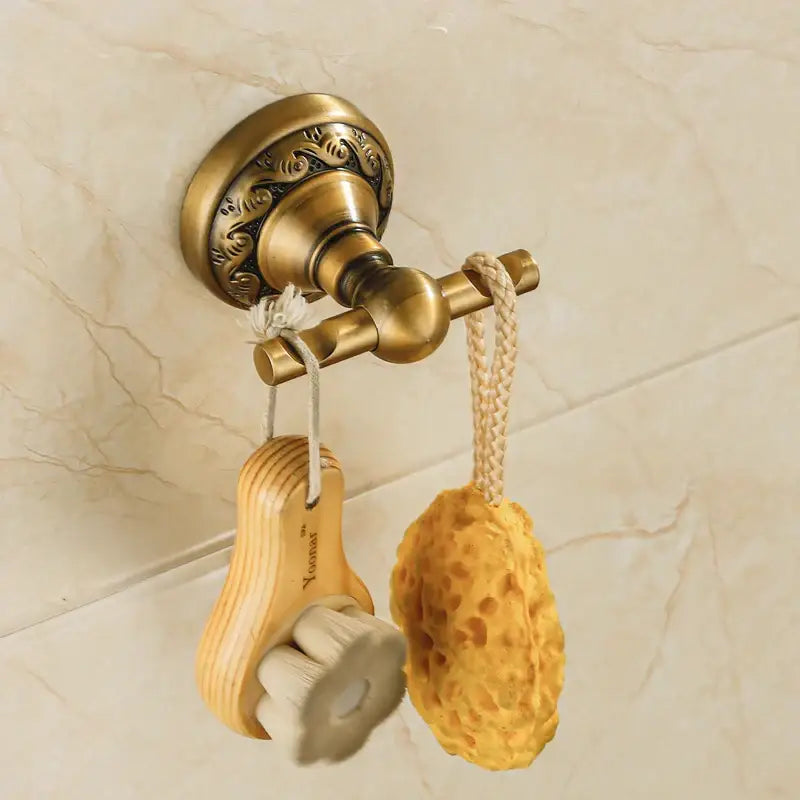 Decorbites™ antique brass robe hook wall-mounted towel rack with ornate detailing holding brush and yellow sponge