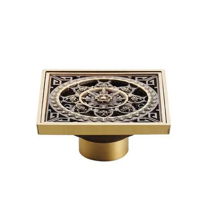 Square antique brass shower floor drain grate with intricate floral and geometric embossed patterns by DecorBites