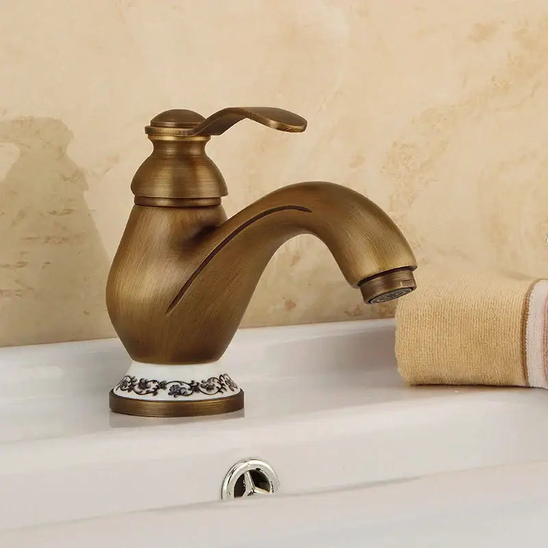 DecorBites antique brass single handle bathroom faucet with ornate white ceramic base featuring black floral detailing