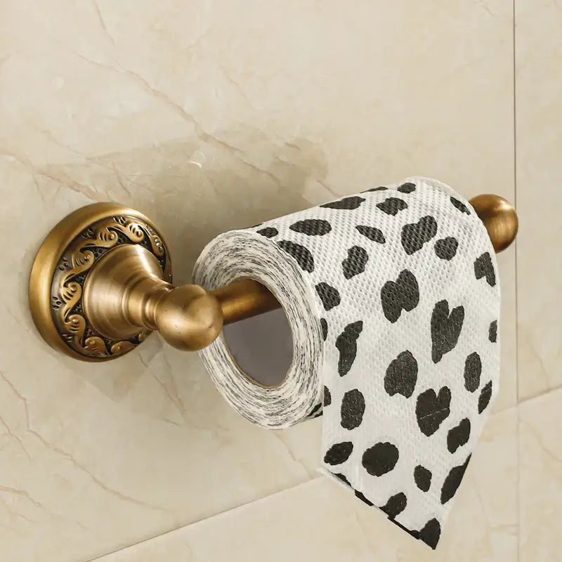 DecorBites antique brass toilet paper holder with ornate detailing holding a roll of white tissue with black hearts