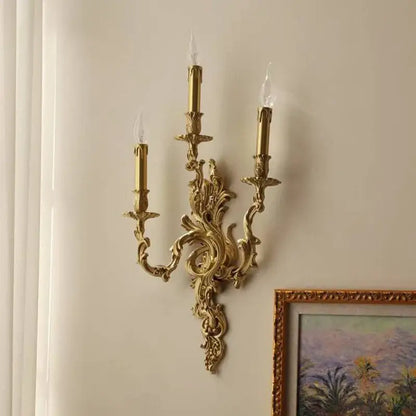 Ornate decorbites antique brass wall sconce with three candle arms and intricate scrollwork in french vintage style