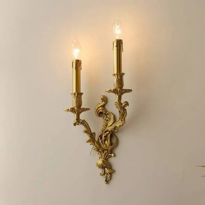 Gold-colored ornate antique brass wall sconce with two candle-style bulbs and intricate floral detailing by decorbites