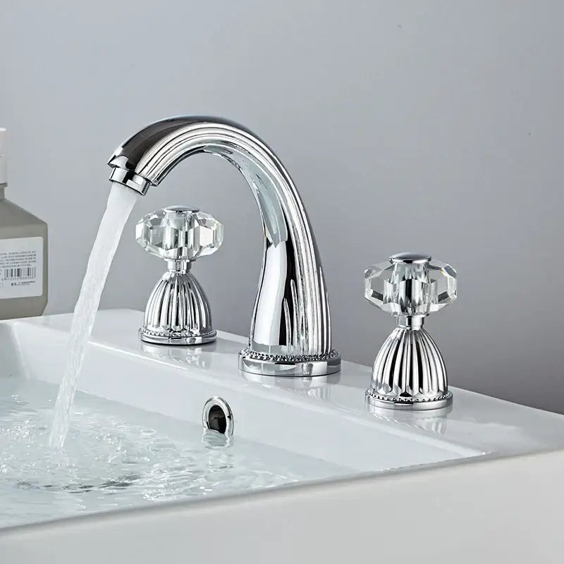 Chrome finished three-handle widespread basin faucet with faceted crystal knobs and curved spout on white sink