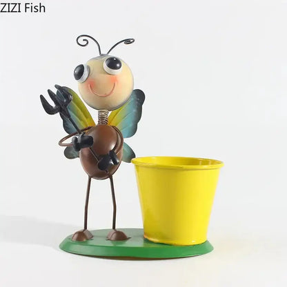 A whimsical metal bee figurine with yellow and blue wings stands beside a bright yellow pot in the decorbites ants gardener vase