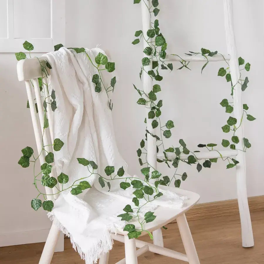 Green silk leaves of decorbites artificial hanging christmas garland draped over a white wooden chair for decoration