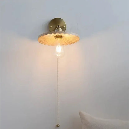 Gold-toned DecorBites ash wood LED wall sconce with scalloped fan-shaped shade and exposed bulb on delicate chain