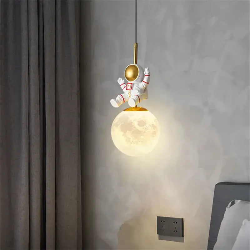 Decorbites astronaut chandelier featuring a white figurine with gold helmet and red accents above glowing moon lamp