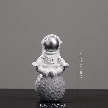 Decorbites astronaut figurine abstract sculpture featuring a white figurine with metallic silver helmet seated on gray moon surface