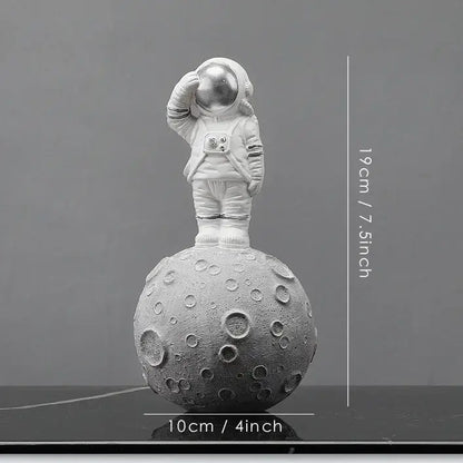 A white decorbites astronaut figurine standing on a textured gray moon surface with one hand raised to helmet