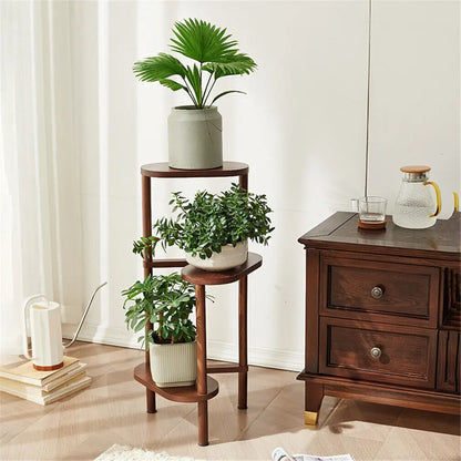 Dark wood bamboo corner plant stand with three circular shelves and slender legs holding green plants in ceramic pots