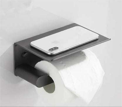 Black metal toilet paper holder with integrated shelf holding a silver smartphone from decorbites bathroom hardware set