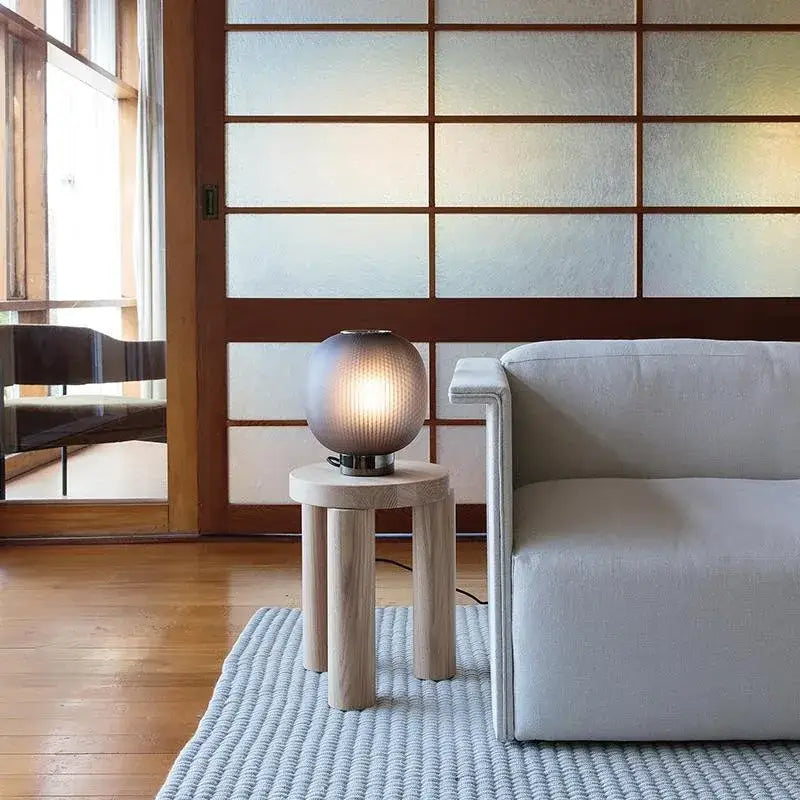 A softly glowing decorbites black glass ball table light with textured surface on a minimalist wooden side table