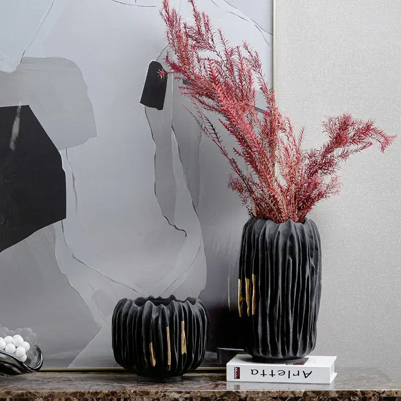 Black ceramic vase with gold crease texture and vertical ridges holding pink dried foliage by DecorBites
