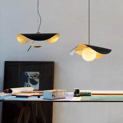 Two decorbites black gold pendant lights with leaf-like glass shades hang above a desk in retro Nordic style
