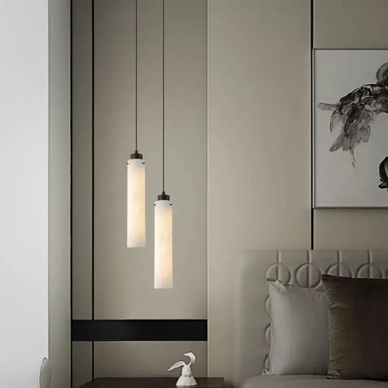 Two slender cylindrical pendant lights with frosted glass shades and black gold marble decorbites fixtures