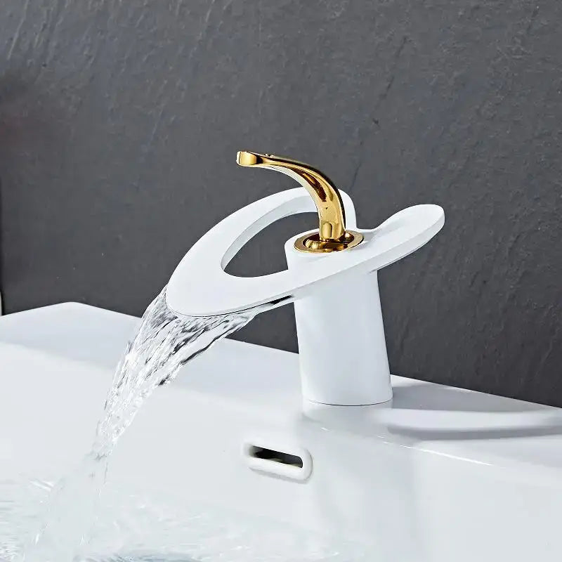 A modern white ceramic waterfall basin faucet with a sleek curved spout and gold-toned handle by DecorBites™