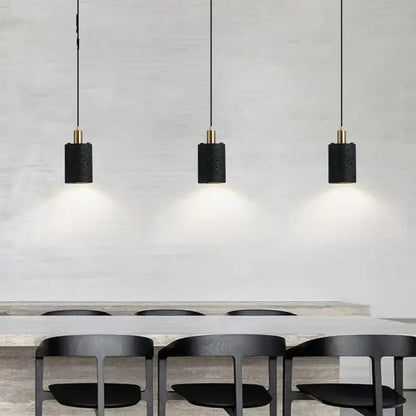 Three black cylindrical pendant lights with textured surfaces and gold accents from decorbites black hole stone chandelier