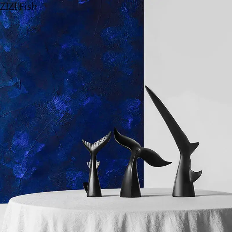 Three sleek black shark tail resin sculptures with glossy finish on white tablecloth against blue backdrop for home decor