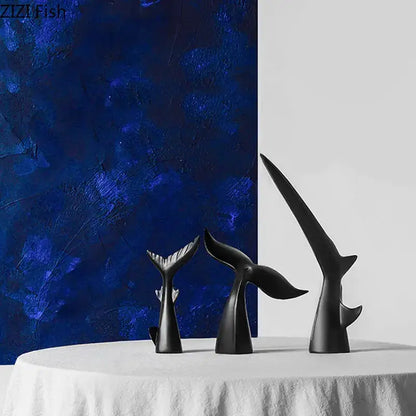Three sleek black shark tail resin sculptures with glossy finish on white tablecloth against blue backdrop for home decor