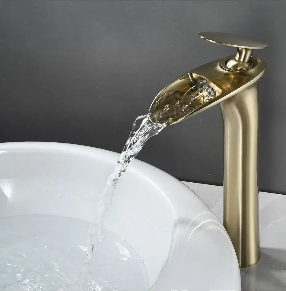 Decorbites™ brass-finished waterfall bathroom faucet with modern design flowing water into white ceramic basin sink