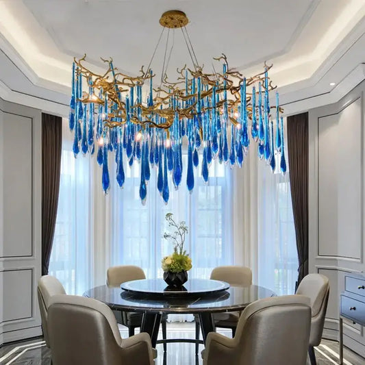 Decorbites blue crystal chandelier with striking blue glass and gold branching arms hanging above dining table
