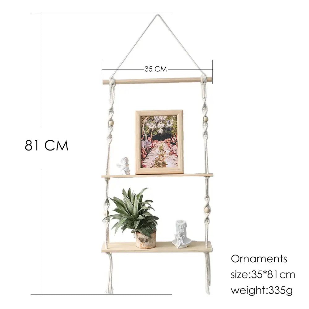 Beige boho macrame wall shelf with three wooden tiers adorned with beads holding photo frame plant and figurines for home decor