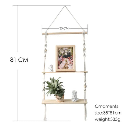Beige boho macrame wall shelf with three wooden tiers adorned with beads holding photo frame plant and figurines for home decor