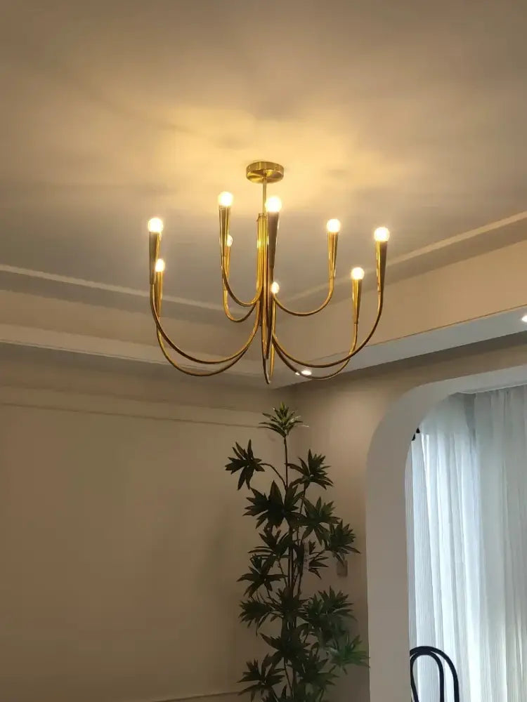 Gold-toned decorbites brass chandelier with multiple curved arms and glowing bulbs for dining room lighting