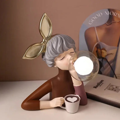 A decorbites bubble girl resin night light of a gray-haired woman blowing a glowing glass bubble holding a white heart mug
