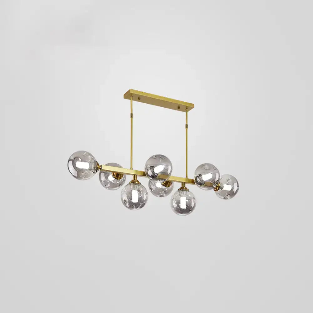 Modern gold-toned pendant light with seven clear glass globe bulbs suspended from a sleek horizontal bar for dining