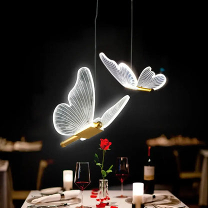 Two illuminated decorbites butterfly led pendant lights with translucent wings and gold bodies hang above dining table