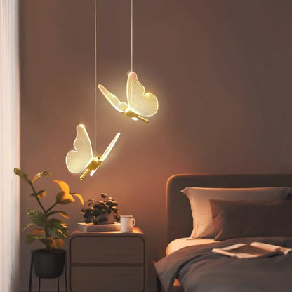 Two elegant decorbites butterfly led pendant lights with glowing translucent wings and gold bodies hang above a bedroom