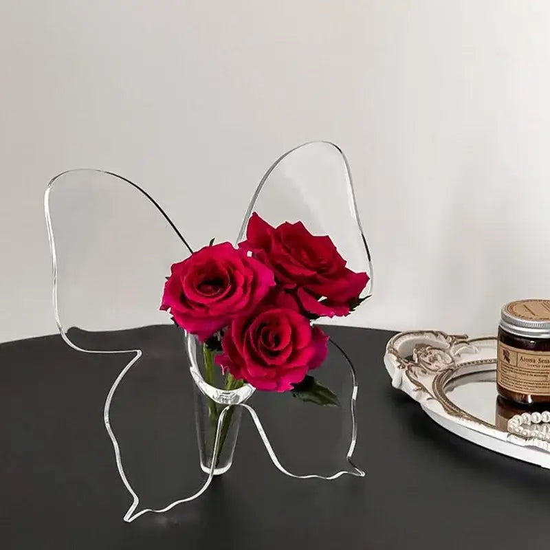 Clear acrylic butterfly vase holding three vibrant red roses for elegant aesthetic room decor by DecorBites™