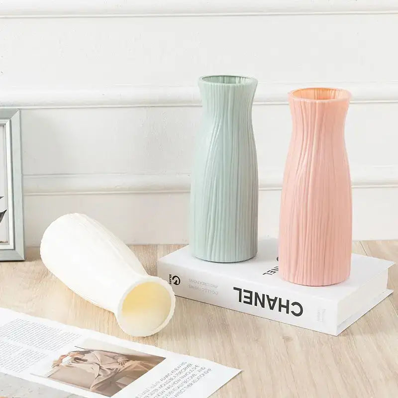 Three slender ribbed plastic vase imitation ceramic flower pots in mint green blush pink and off-white on a wooden surface
