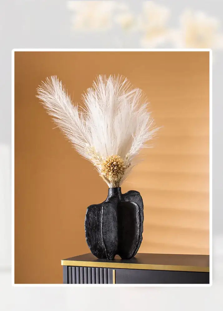 Black textured ceramic sea vase by decorbites holding white feathery dried flowers with a central golden sphere in nordic modern style