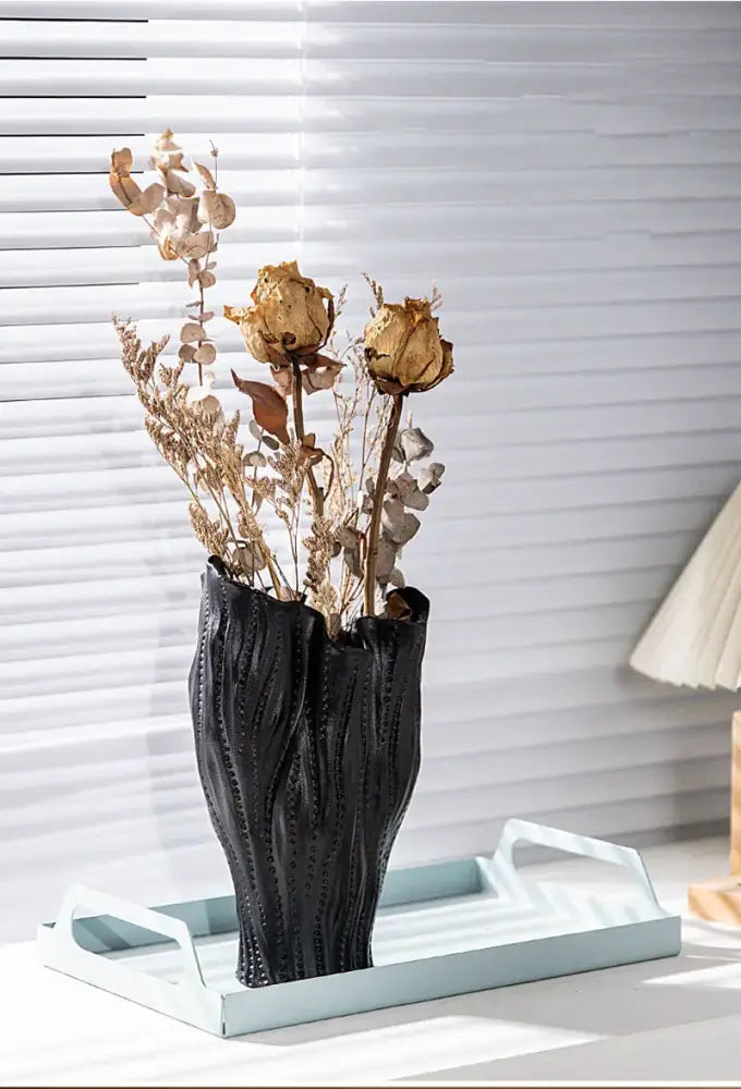 Black ceramic sea vase with textured ribbed surface holding dried golden roses and eucalyptus nordic modern decor