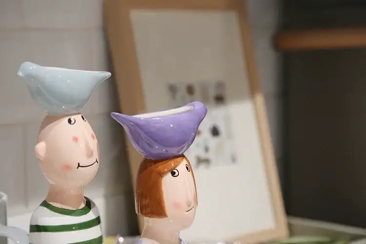 Two ceramic figurines in striped shirts balancing colorful bird-shaped bowls in a decorbites ceramic vase set for home decor