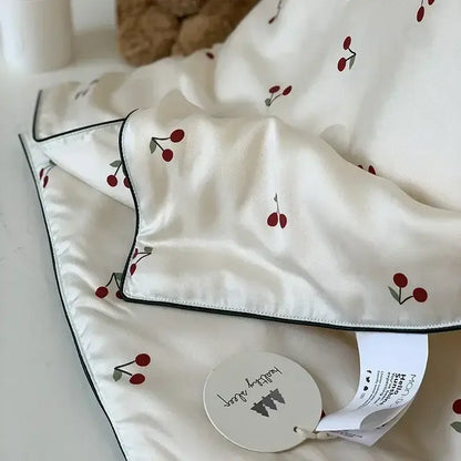 A soft white satin decorbites cherry lyocell fiber cooling blanket with red cherries green stems and black piping edges