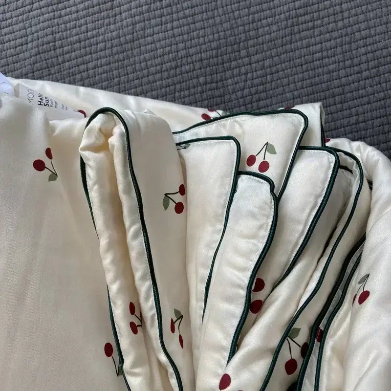 Cream-colored satin quilt with red cherry embroidery and dark green piping from decorbites cherry lyocell fiber cooling blanket