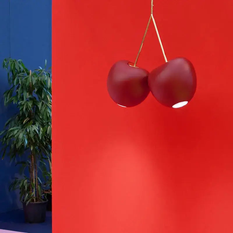A pair of glossy red decorbites cherry pendant lamps with gold stems hanging against a vibrant red wall