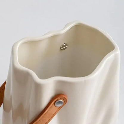Cream-colored chic ceramic vase with a wavy rim and tan leather strap for elegant home decoration by DecorBites