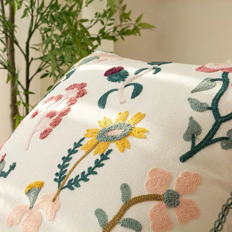A cream-colored decorbites chic floral geometric cushion cover featuring intricate pink yellow and green floral embroidery