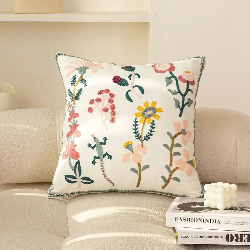 A square white decorbites chic floral geometric cushion cover with colorful embroidered flowers and a green lizard