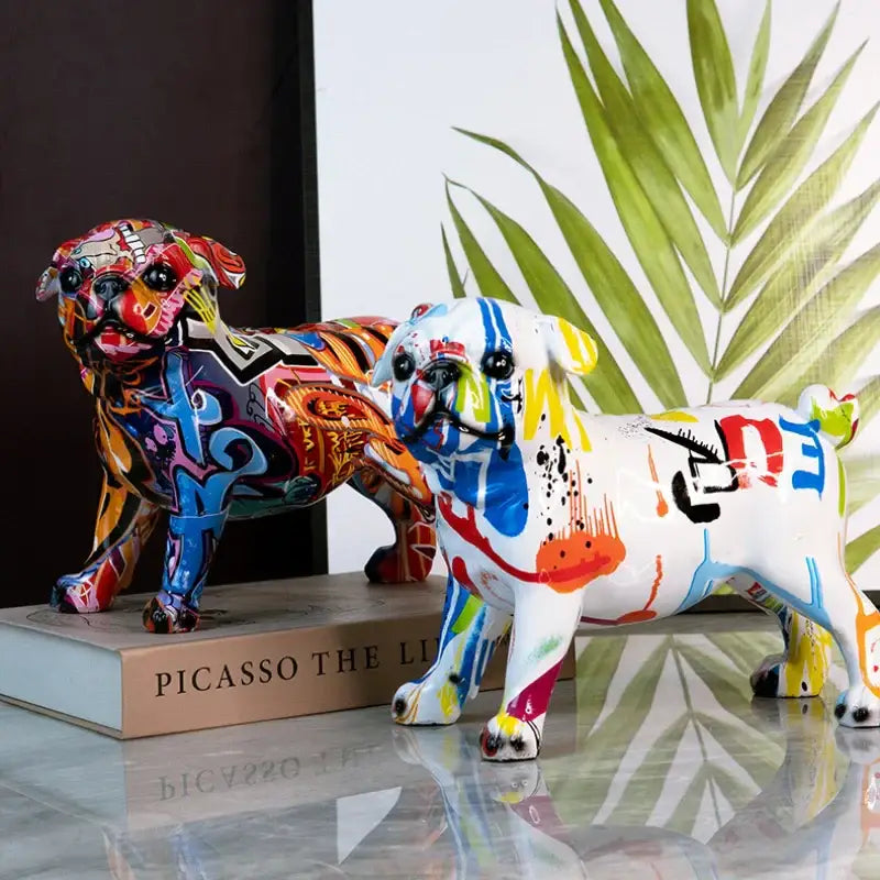 Two vibrant graffiti-style pug figurines featuring bold blue red yellow and black splash color art on glossy resin surfaces decorbites chihuahua splash statue