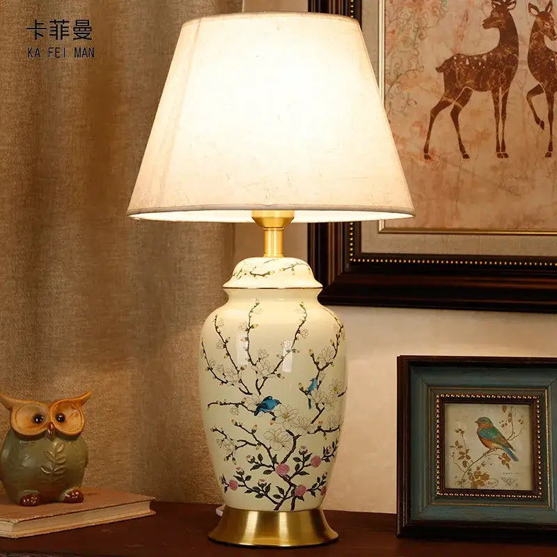 Cream-colored ceramic table lamp by DecorBites with hand-painted blue birds and pink blossoms, gold-toned base