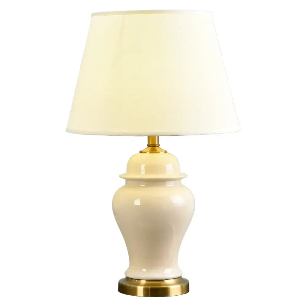 Cream-colored ceramic table lamp with gold metal base and off-white shade for living room or bedroom decor