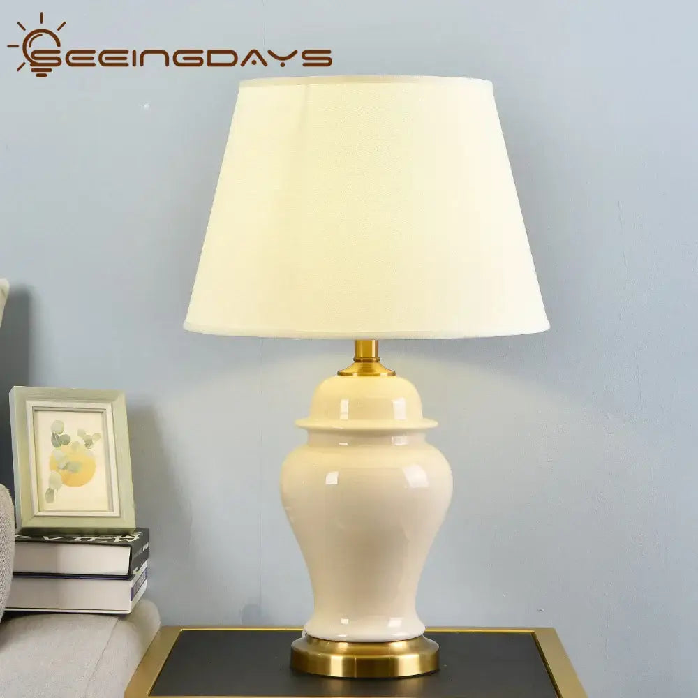 Cream-colored ceramic table lamp with gold-toned metal base and off-white fabric shade for living room decor