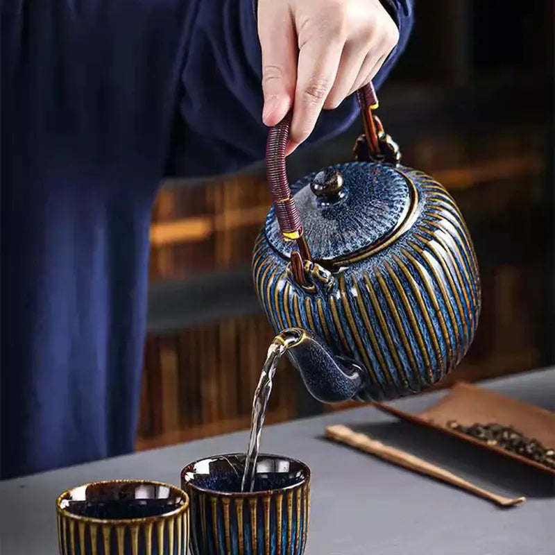Glossy blue ceramic teapot with gold-striped ridges being poured by hand from decorbites ceramic teapot set