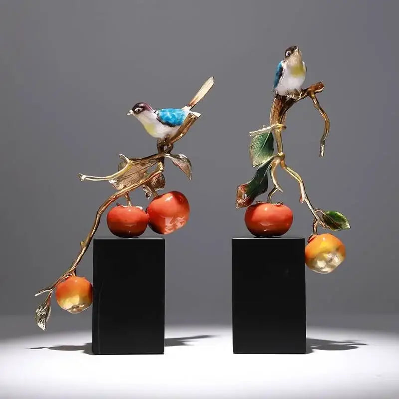 Two enamel persimmon ruyi ornaments featuring blue and white birds on golden branches with red persimmons on black bases