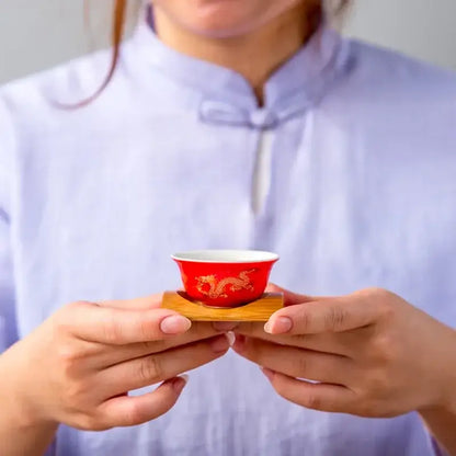 A vibrant red porcelain ceramic tea cup with golden dragon design held gently, perfect for dragon tea cup use